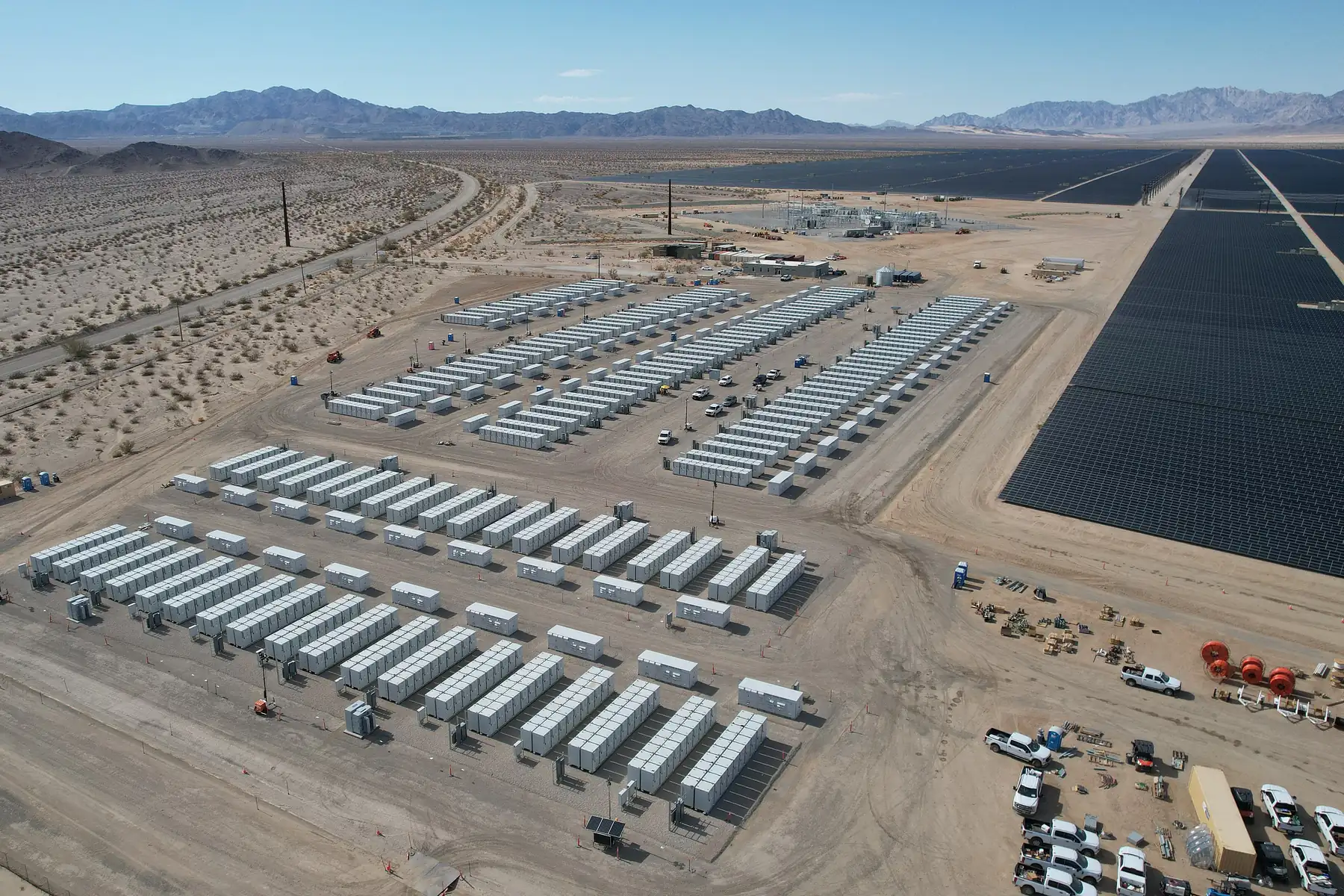 Rows of battery storage containers beside a solar field at the Desert Sunlight project in California's Mojave Desert