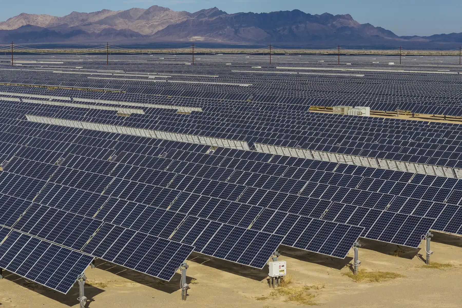 Rows of solar panels at a utility-scale solar project in Riverside County, California, with desert mountains behind