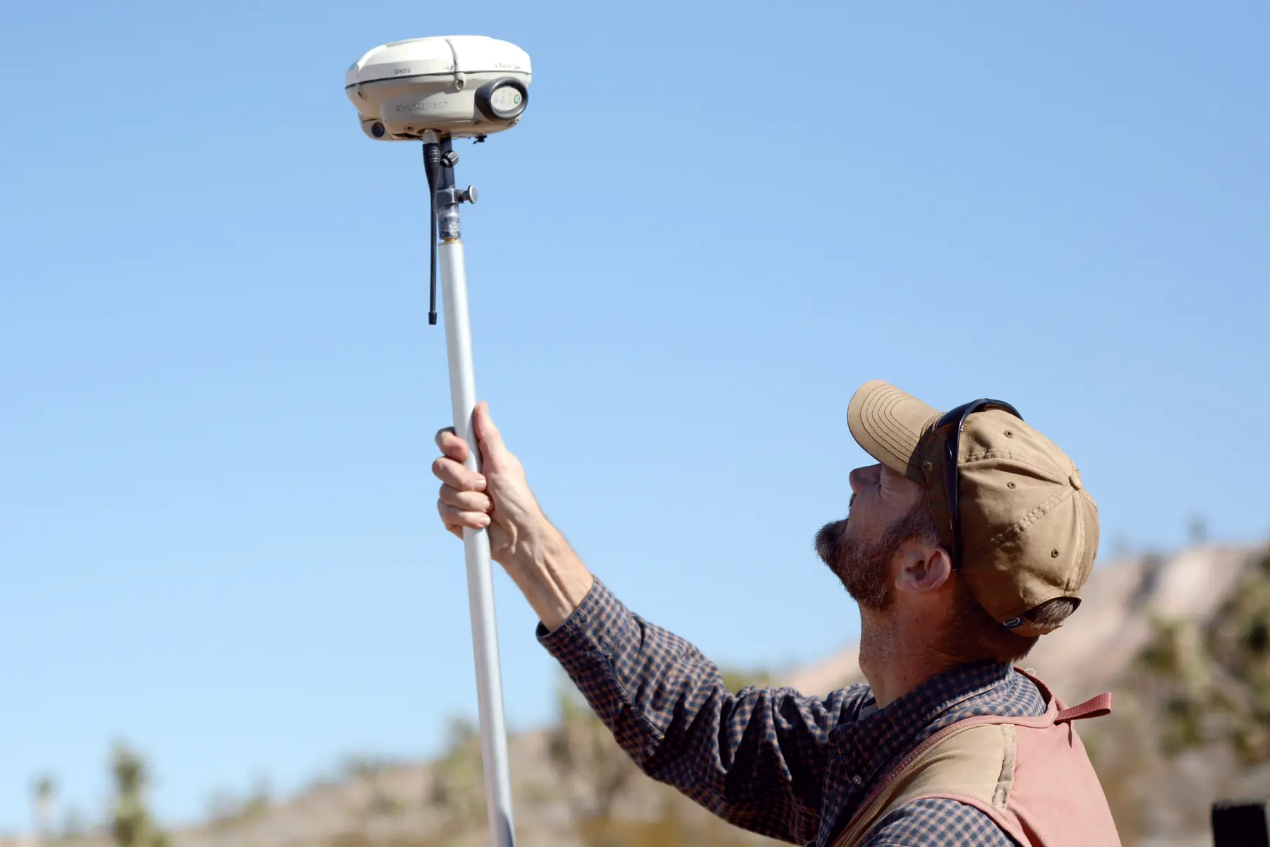 A land surveyor raises a GNSS receiver on a survey pole during a boundary re-survey